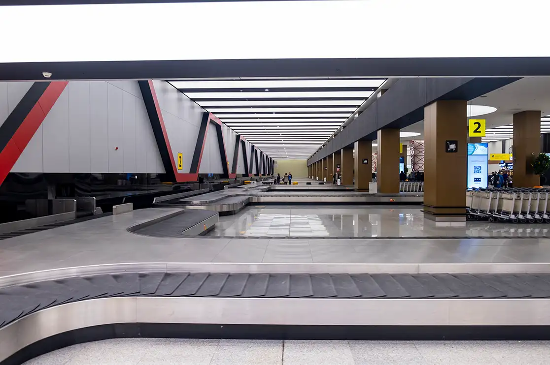 Airport baggage claim hall with conveyor belts, structural columns, overhead lighting, and luggage trolleys