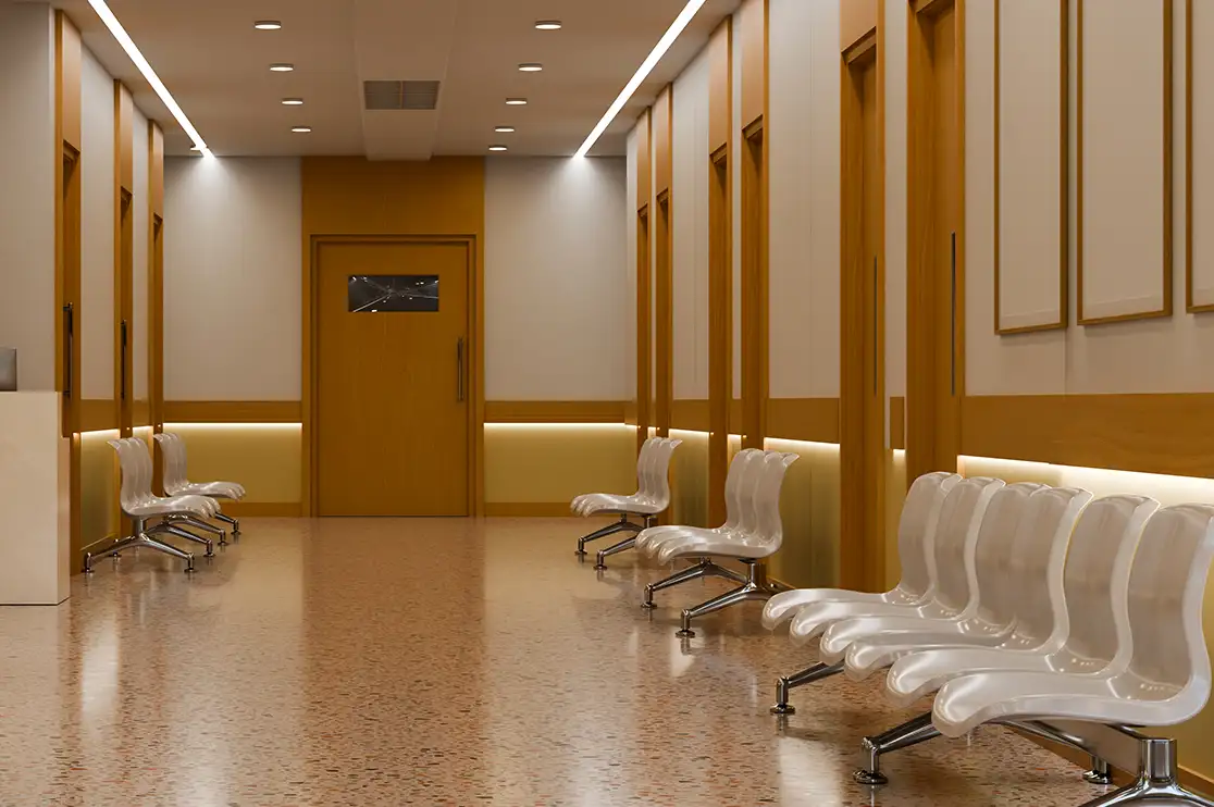 Hospital corridor with wood-finish wall paneling, integrated lighting, framed wall panels, and patient waiting chairs.