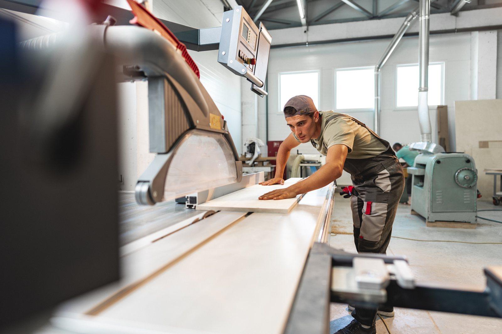 Worker guiding a panel through a beam saw on the shop floor of a furniture factory