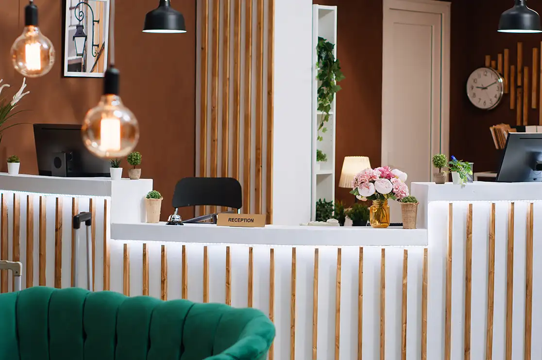 Interior reception area featuring custom millwork counters with vertical wood slat detailing, integrated workstations, pendant lighting, and decorative finishes