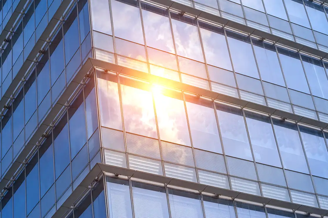 Close-up of a modern skyscraper's glass facade, highlighting reflective glazing, exterior panel details, and sunlight reflecting off the building's surface.