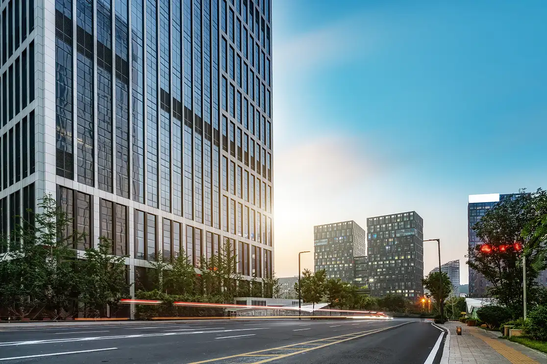 Street-level skyscraper rendering showcasing a modern glass high-rise facade, landscaped sidewalks, surrounding office buildings, and an urban streetscape in warm evening light.