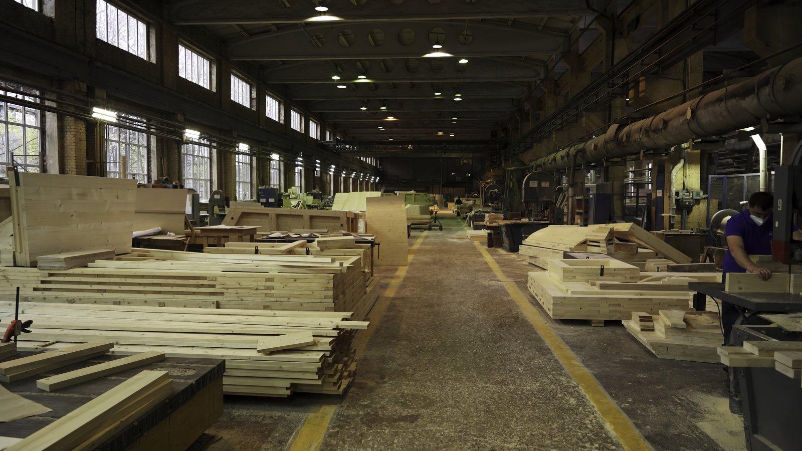 Woodworking shop floor with stacked lumber and workstations along both sides